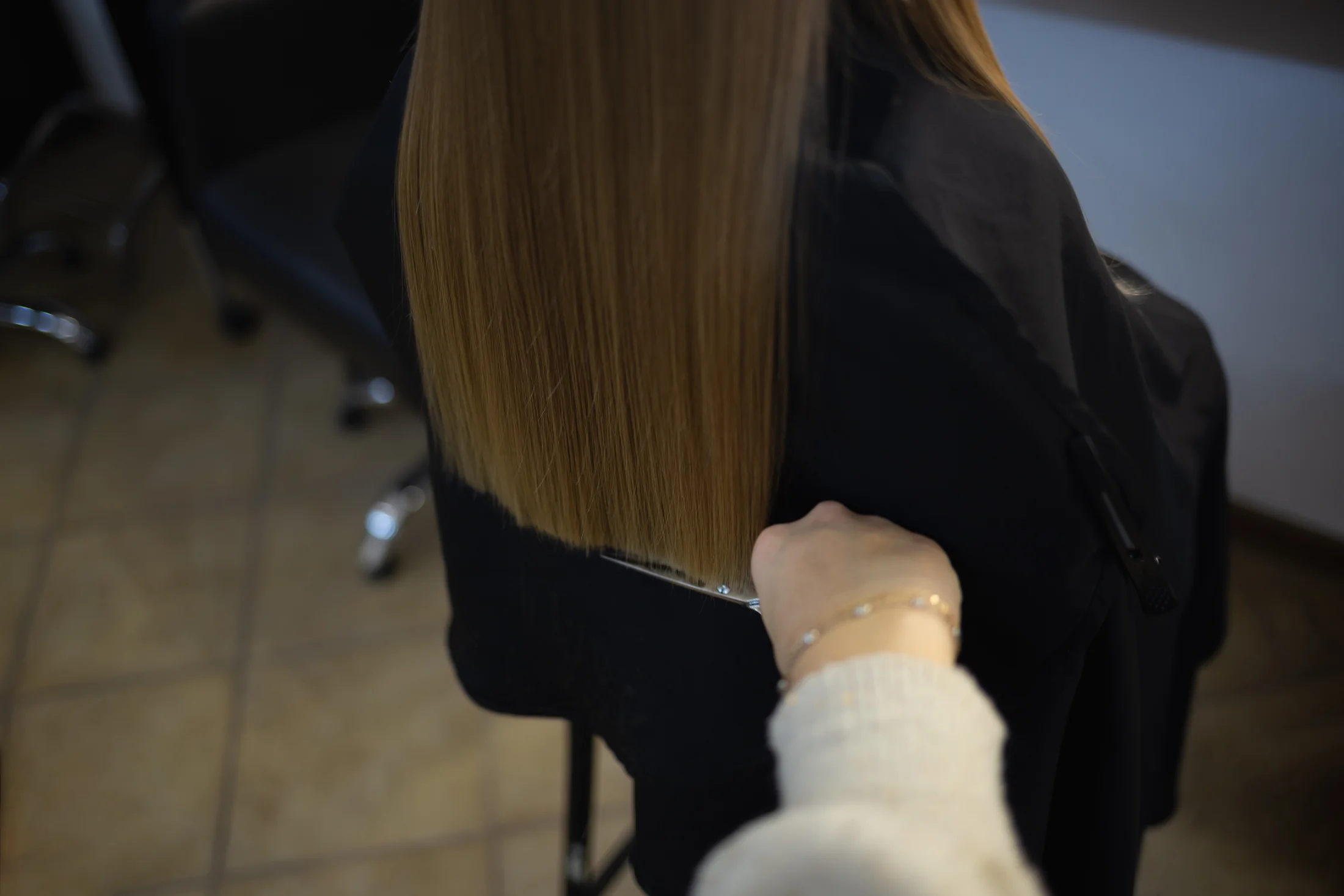 Close-up of scissors trimming straight hair, viewed from behind