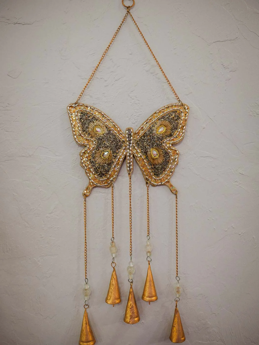 A gold butterfly chime hanging on a white wall