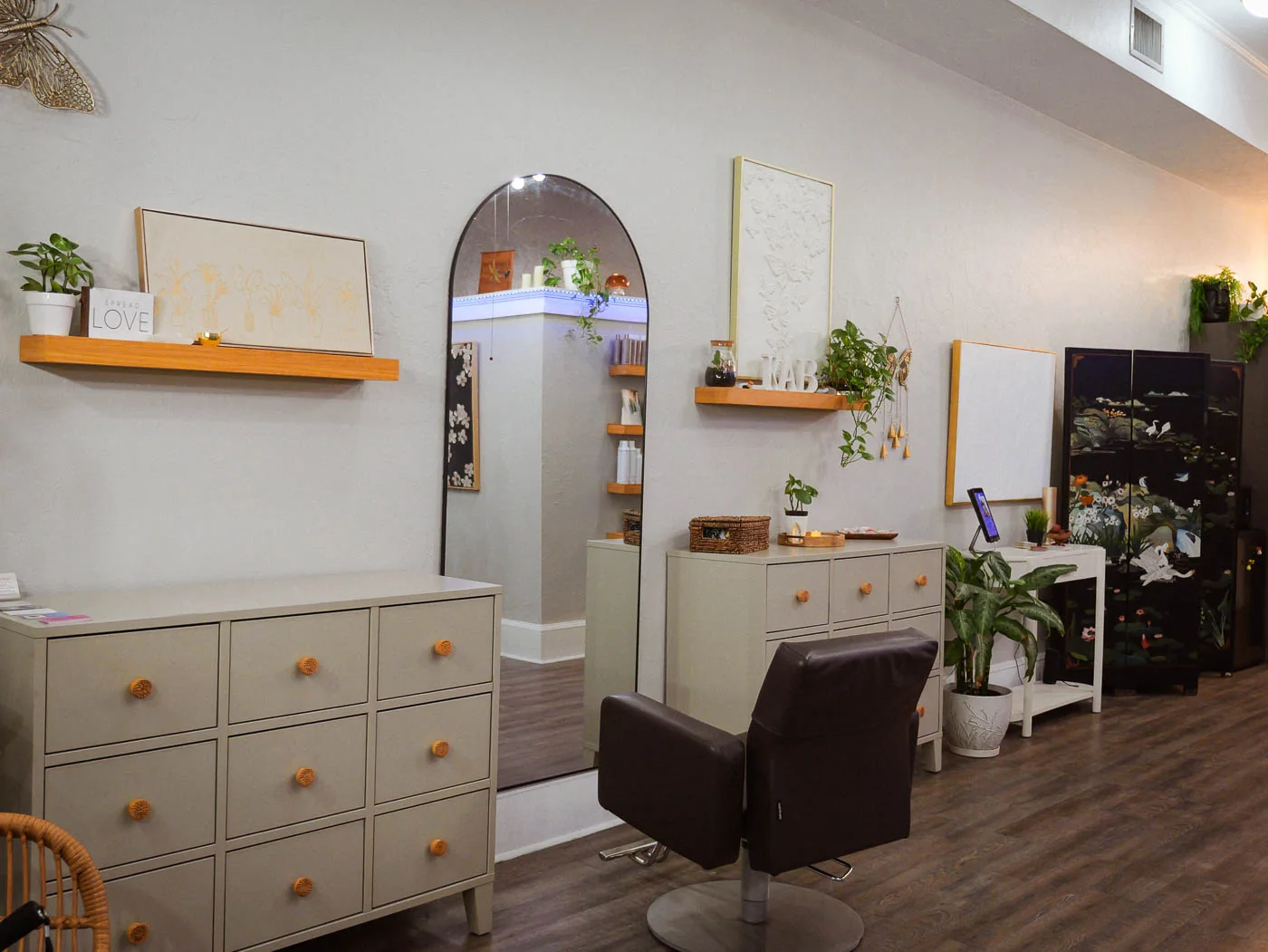 A styling chair and arched mirror beside a cream cabinet